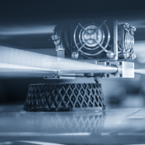 Impressora 3D em operação com bico, ventiladores e superfície de impressão.